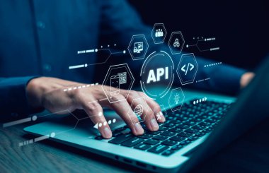 Teknoloji aygıtı internetin arka planında API simgesi olan bir dizüstü bilgisayar kullanan işadamı, API Uygulama Programlama Arayüzü internet veri iletişiminde servisleri birbirine bağlar.
