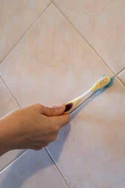 A Woman's hands cleaning the joint of the tiles with a toothbrush. Vertical orientation.