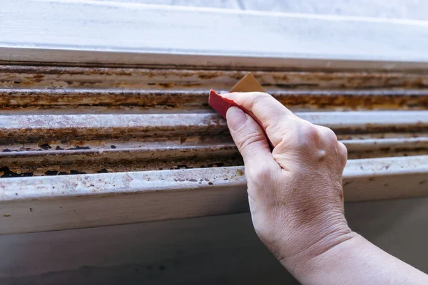 An Hands of a woman with a sandpaper sanding a window frame before painting. Empowered woman concept.