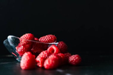 Normal view of a Serving of Raspberries in a small clear bowl on a black granite surface. Horizontal orientation, space for text.