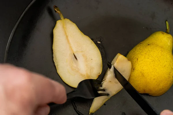 A Sliced yellow pear on a black plate with a bite pricked on a fork.