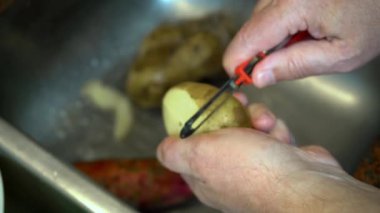 Mutfak lavabosunda patates soyan bir adamın elleri..
