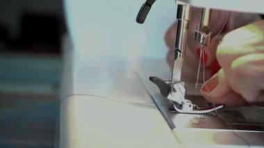 Yaşlı bir kadının elleri dikiş makinesinin iğnesini ipliğe geçiriyordu..