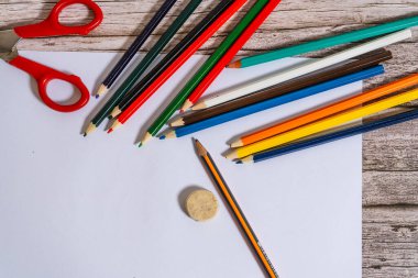 Tahta masadaki beyaz bir çarşafın yanında renkli kalemler..