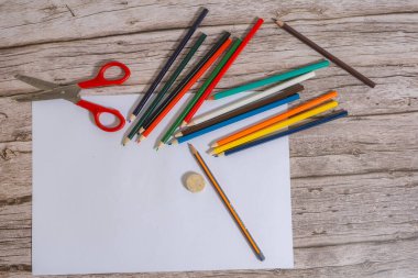 Tahta masadaki beyaz bir çarşafın yanında renkli kalemler..