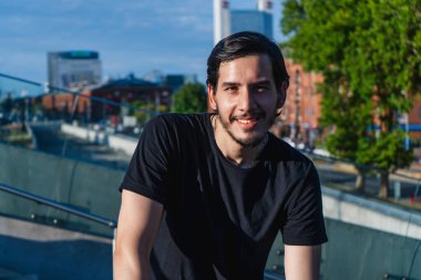 Genç Latin adam gülümsüyor. Şehirde sakin ve sakin.