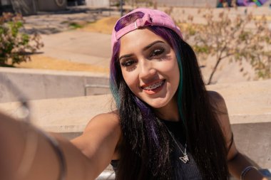 Gülümseyen bir milenyum kadını sokakta selfie çekiyor.