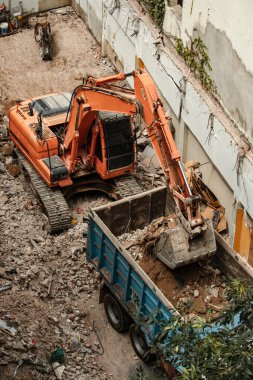 Kazıcı yıkım alanından enkazı kaldırıyor ve bir kamyonun arkasına boşaltıyor.