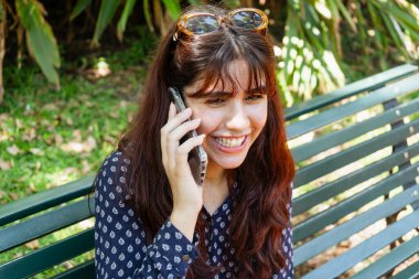 Genç bayan akıllı telefonunu kullanıyor, parkta hoş bir sohbetin tadını çıkarıyor.