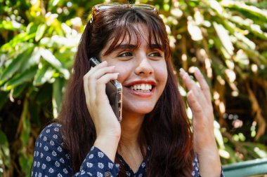 Genç bayan akıllı telefonunu kullanıyor, parkta hoş bir sohbetin tadını çıkarıyor.