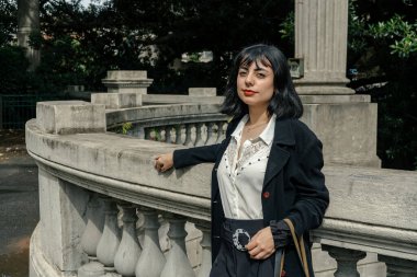 Klasik bir şehir parkı ortamında poz veren şık İspanyol kadın zarafet ve kendine güven sergiliyor.