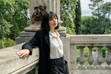 Klasik bir şehir parkı ortamında poz veren şık bir iş kadını, sakin atmosferin tadını çıkarıyor.