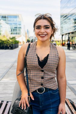 Modern bir şehir ortamında kendinden emin bir şekilde gülümseyen genç kadın.