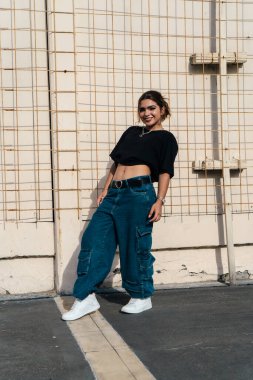 Tarz sahibi bir kadın, dokulu bir duvara karşı güvenli bir şekilde poz veriyor.