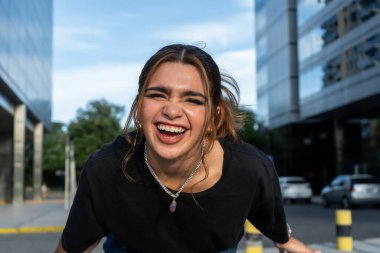 Neşeli kadın modern binalar arasında enerjik bir şekilde gülüyor.