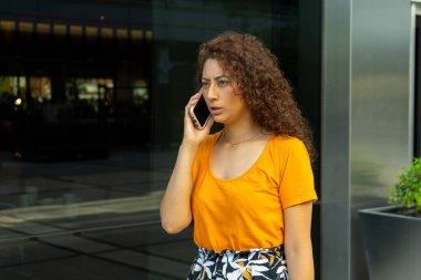 Genç bir kadın telefonda konuşurken şok ve endişeyle tepki veriyor.