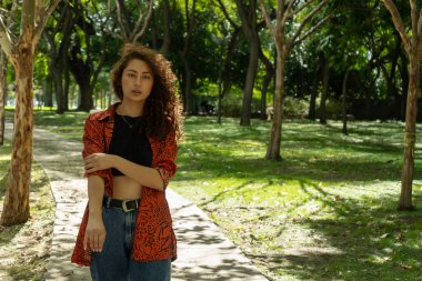 Parkta günlük giysiler içinde yürüyen genç Latin kadın.