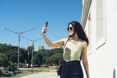 Buenos Aires, Arjantin 'deki bir parkın yakınlarında yürürken akıllı telefonuyla selfie çeken genç bir kadın.