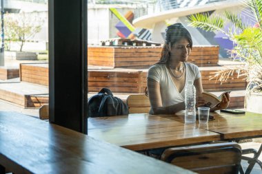 Genç Latin bir kadın kafeteryada kitap okuyarak sakin bir anın tadını çıkarıyor.