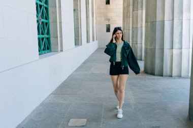 Genç İspanyol kadın telefonda konuşurken zarif bir şehir galerisinde yürüyor.