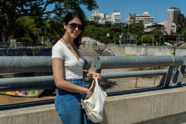 Şehirli bir parkta güneşli bir günün tadını çıkarırken çantasında bir şey arayan şık genç bir kadın.