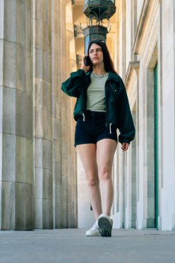 Süslü genç Latin kadın koridorda yürüyor ve telefonda konuşuyor.