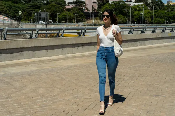 Şık bir kadın şehirde güneşli bir günde yürüyüş yapıyor.
