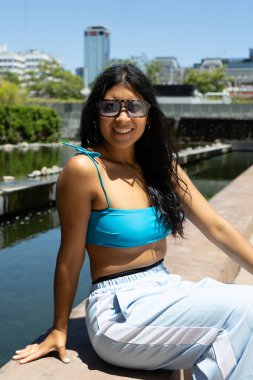 Genç Latin sporcu kadın güneşli bir günde şehir dışında egzersiz yaptıktan sonra havuz kenarında dinleniyor.