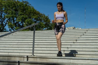 Formda bir kadın şehir ortamında merdivenleri tırmanarak fiziksel durumunu iyileştiriyor.