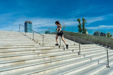 Kadınlar açık mavi bir gökyüzünün altında merdivenlerden koşarak egzersiz yaparlar.