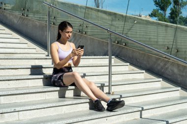Dışarıda merdivenlerde oturan bir kadın akıllı telefon kullanıyor.