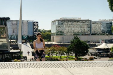 Şehir parkında koşan genç bir kadın sağlıklı yaşam tarzını sürdürüyor.