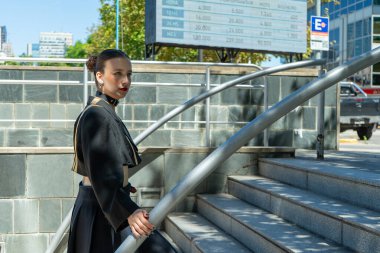 Modern siyah takım elbiseli bir iş kadını şehir ortamında metal parmaklıklarla merdivenleri tırmanıyor.