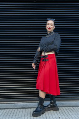 Moda mankeni, modaya uygun bir elbise, kırmızı etek ve siyah bluzla modern bir siyah arka plana karşı poz veriyor.