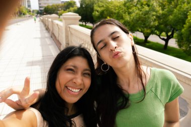 İki mutlu kadın selfie çekiyor barış işareti yapıyor ve öpüşüyorlar.