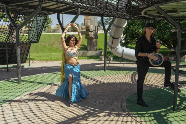 Güneşli bir parkta bir darbuka oyuncusuyla bir odalisk arasında mistik bir dans