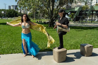 Güneşli bir parkta bir darbuka oyuncusuyla bir odalisk arasında mistik bir dans