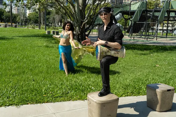 Güneşli bir parkta bir darbuka oyuncusuyla bir odalisk arasında mistik bir dans