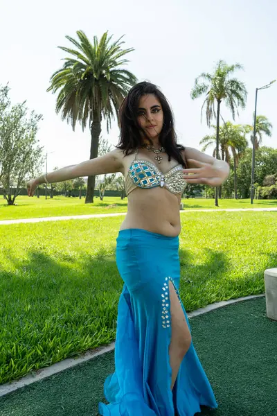 Açık mavi elbiseli güzel bir Arap dansçı parkta dans ediyor.