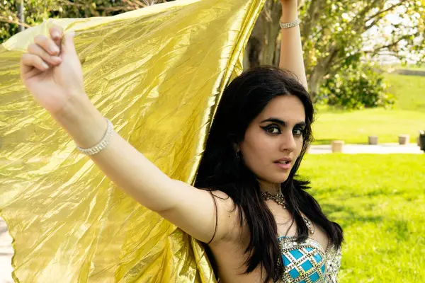 Rüzgarda altın eşarbı olan mavi elbiseli bir Arap dansçı.