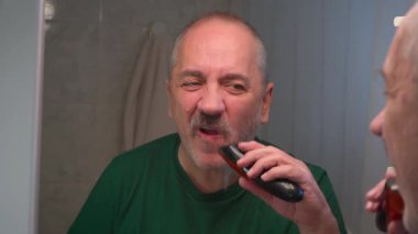 Yetişkin bir adam uzun gri sakalını elektrikli jiletle tıraş ediyor..