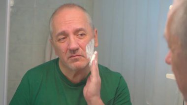 Yetişkin bir adam tıraş köpüğüyle tıraş olmadan önce tıraş köpüğü sürüyor..