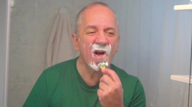 Yetişkin bir adam, bıyığını ve sakalından geriye kalanları tıraş köpüğüyle kaplamak için yüzünü tıraş bıçağı ile kapatıyor..