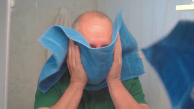 Yetişkin bir adam evinin banyosunda yüzünü havluyla kurutuyor..