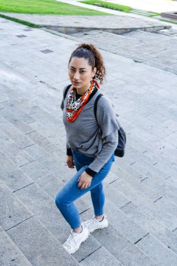 Sırt çantalı genç bir kadın şehir ortamında merdivenlerden iniyor.