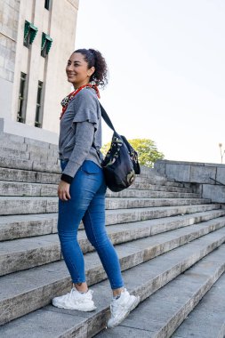 Sırt çantalı genç bir kadın şehir ortamında taştan bir merdivene tırmanıyor. Bu da bir yolculuk ya da seyahat olduğunu gösteriyor.