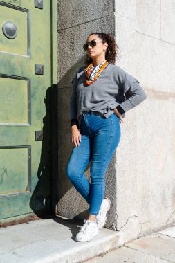 Güneş gözlüğü takan şık bir kadın ve şehir sokaklarında duvara yaslanmış bir eşarp.