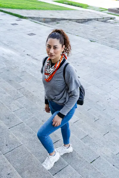 Sırt çantalı genç bir kadın şehir ortamında merdivenlerden iniyor.