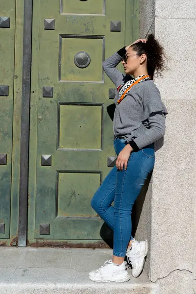 Güneş gözlüğü takan şık bir kadın ve şehir sokaklarında duvara yaslanmış bir eşarp.