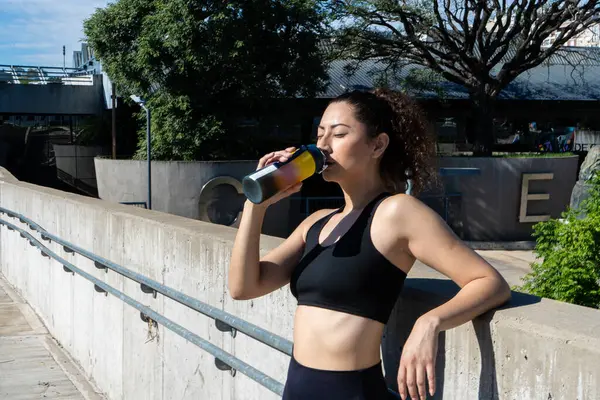 Açık hava eğitiminden sonra su şişesinden su içen genç bir kadın.